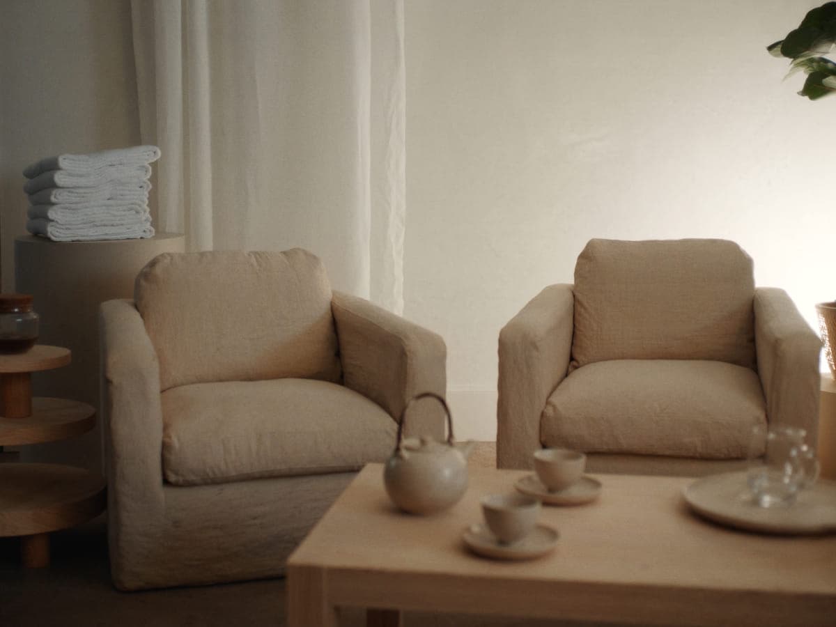 Lounge with two linen armchairs, a low timber table and a pot of tea