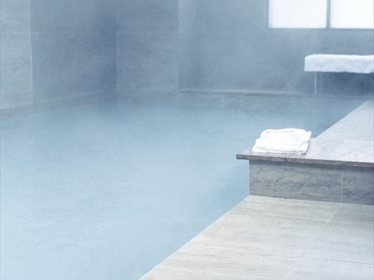 Cold plunge pool, still water and pale stone, towels folded on the ledge